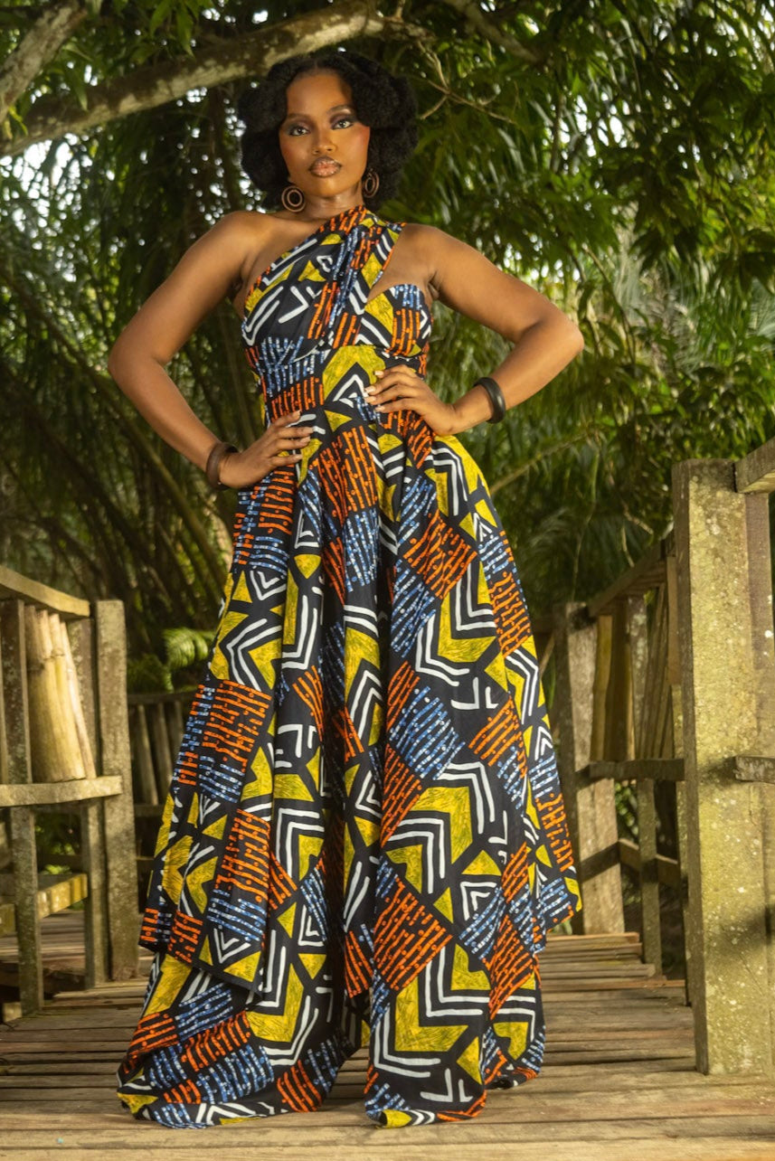 Woman in a colorful African dress standing on a wooden bridge in a forest setting
